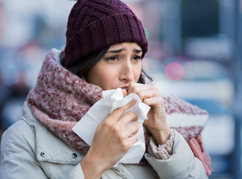 A young woman, wrapped up in winter clothes, is coughing into a tissue
